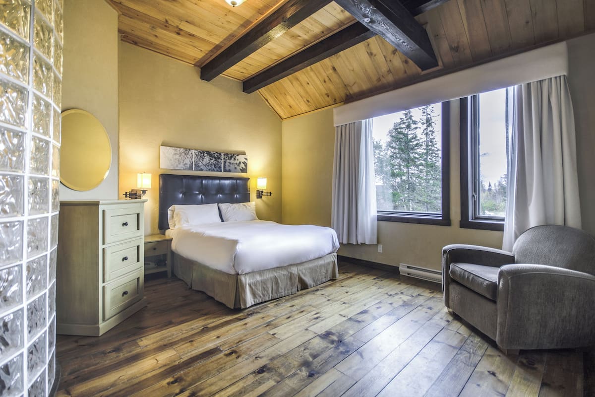 A bedroom with a bed, bedside table, lamp, chair, and a window with curtains.