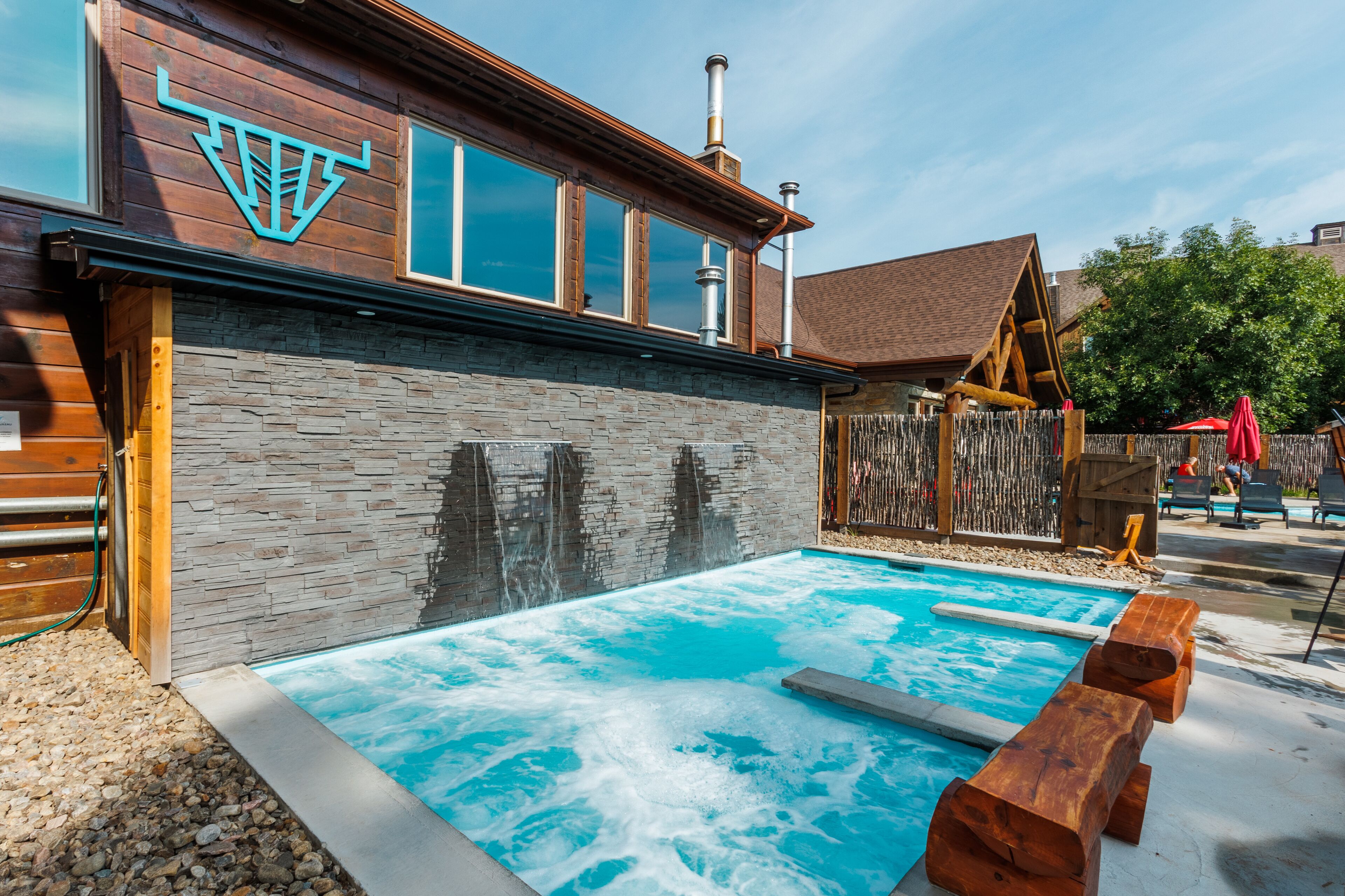 Ein Poolbereich mit Holzterrasse, Steinmauer und großem Fenster.