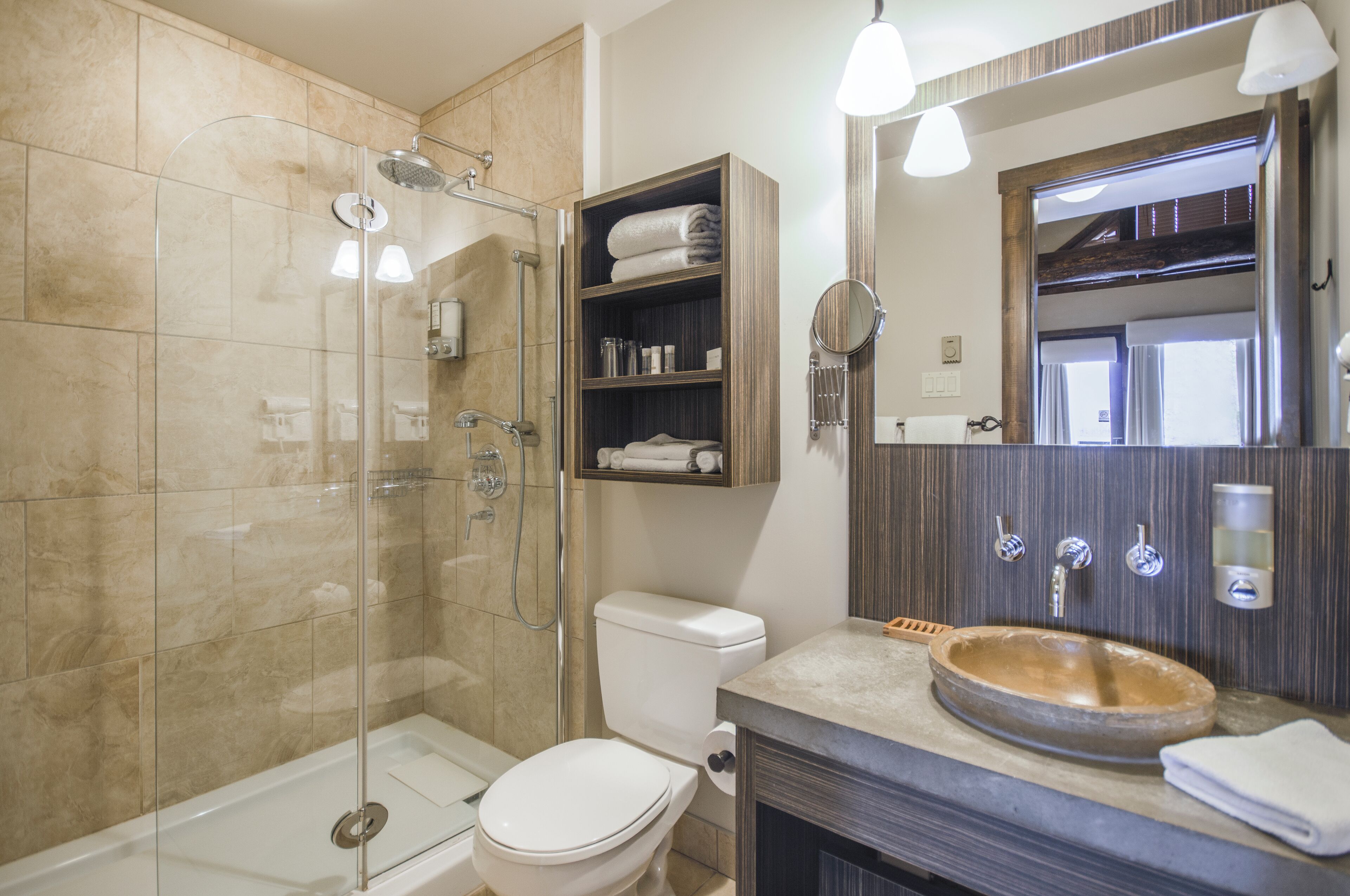 A modern bathroom with a glass-enclosed shower, a toilet, a sink with a wooden basin, and a mirror with a wooden frame.