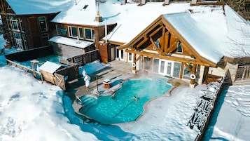 Zona de piscina exterior cubierta de nieve, con estructuras de madera y un jacuzzi.