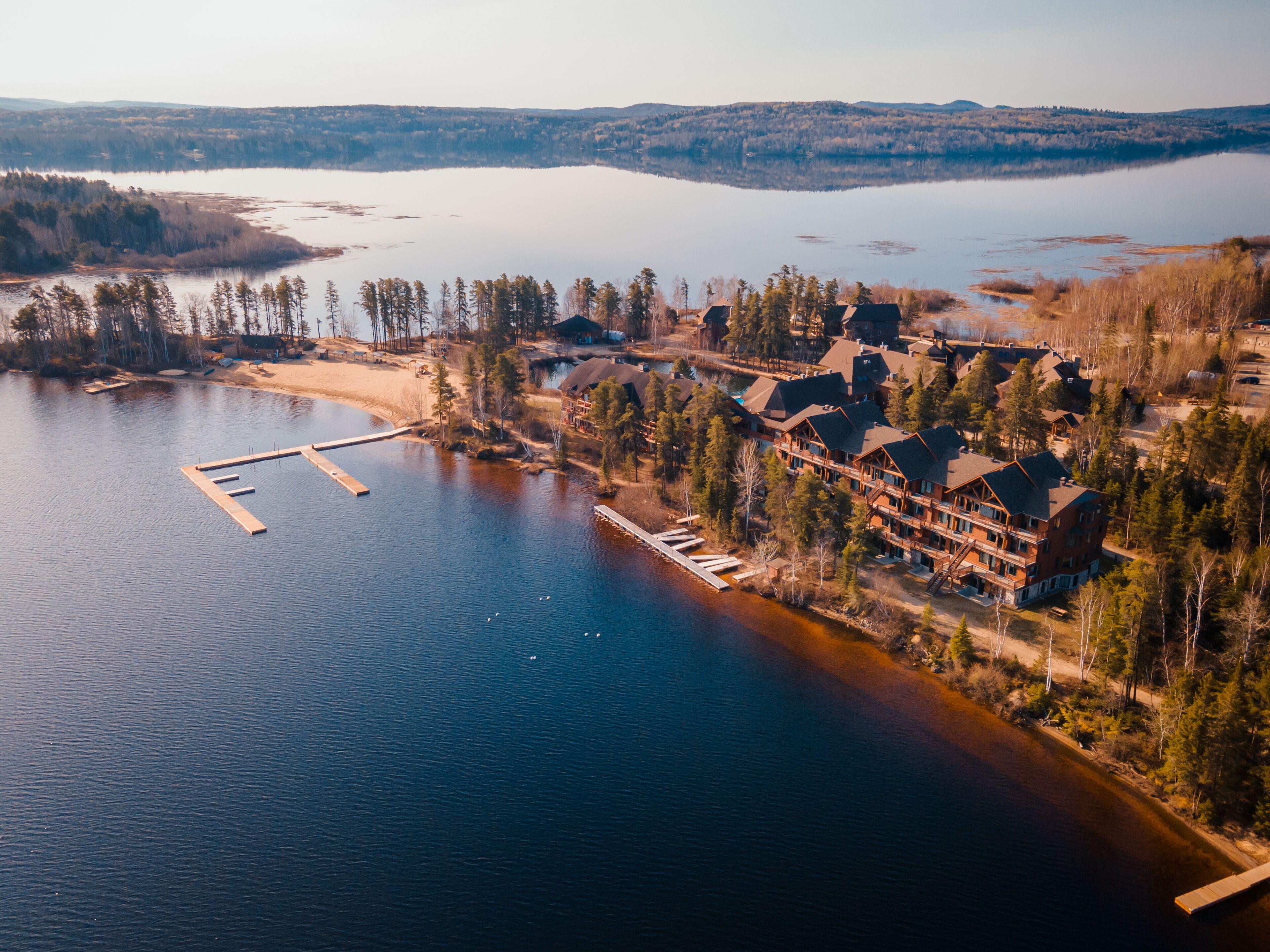 An aerial view of a lakeside lodge with multiple buildings, dock, and surrounding forest.