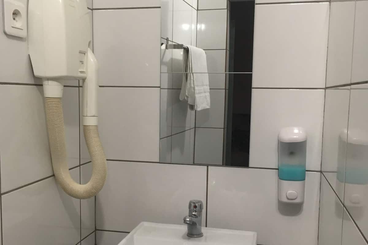 A bathroom with a white sink, a hand dryer, a towel rack, and a soap dispenser.