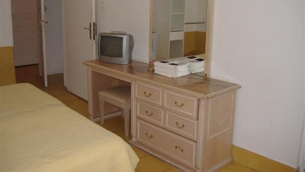 Un dormitorio con cama, cómoda con cajones, televisor y espejo.