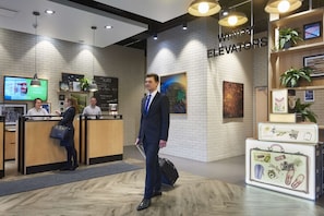 A hotel reception area with a modern design, including a reception desk, a digital screen, and a wall-mounted sign for elevators.