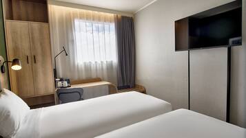 A hotel room with a bed, a desk with a chair, a TV, and a wardrobe.