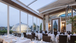 Un restaurante con mesas dispuestas para comer, ventanas amplias y vistas a una estructura en forma de cúpula.