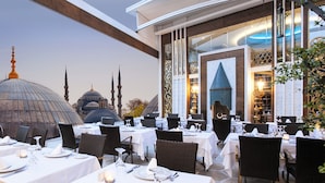 Un restaurante con mesas dispuestas para comer, con vistas a una gran cúpula y minaretes al fondo.