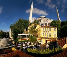Ein Innenhof mit Außenbestuhlung, ein gelbes Gebäude und eine Moschee mit zwei Minaretten im Hintergrund.