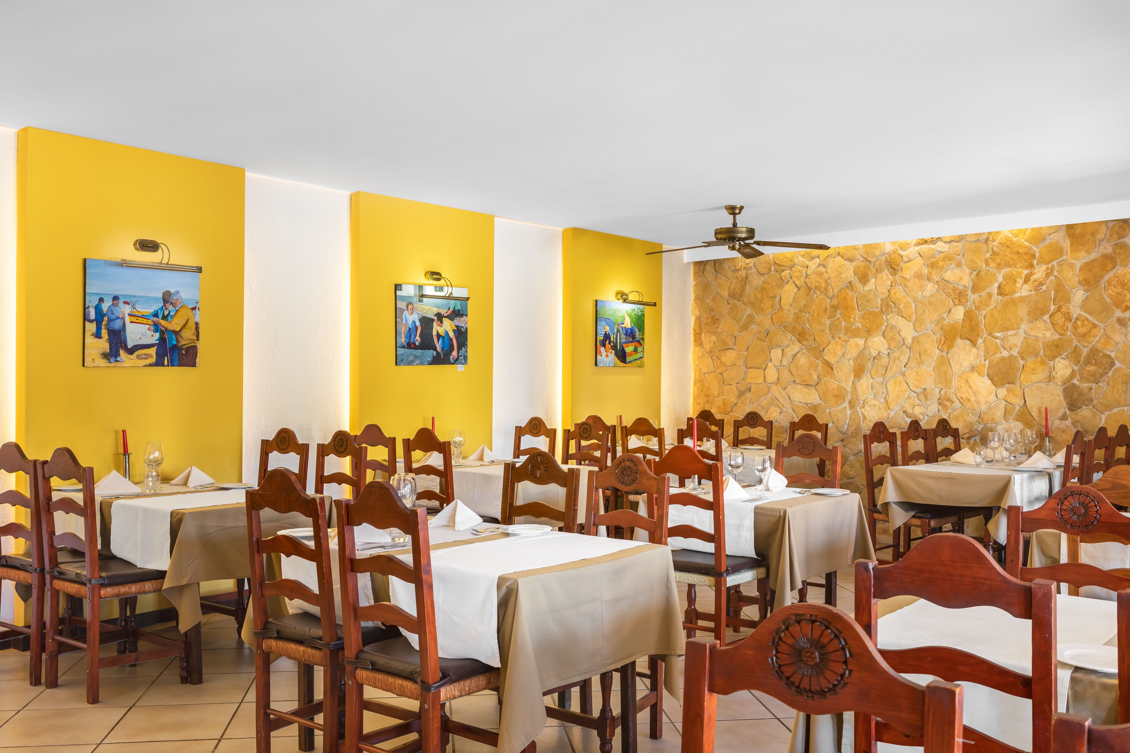 Un restaurant aux murs jaunes, avec des chaises et des tables en bois, disposées pour le service.