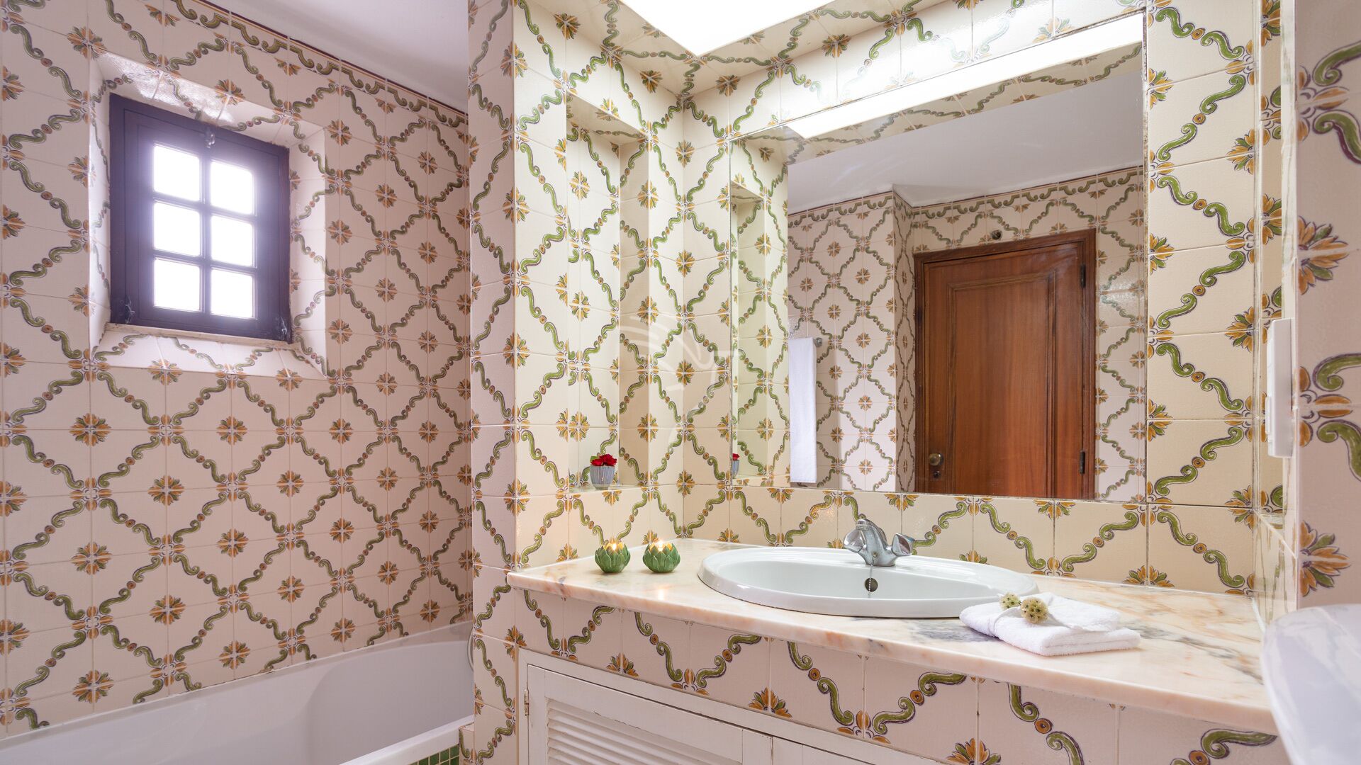 A bathroom with patterned tiles, a bathtub, a sink with a mirror, and a window.