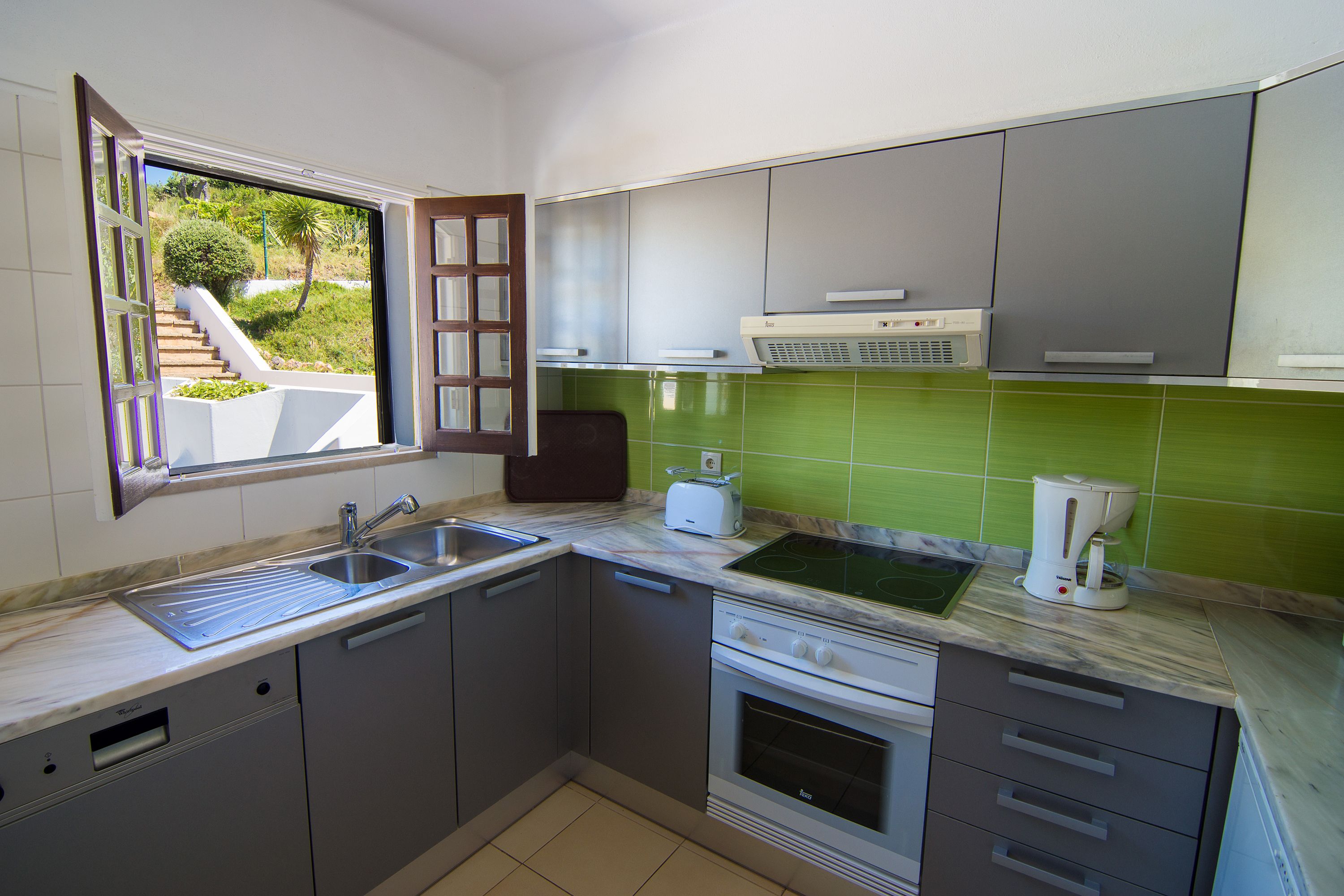 A kitchen with a built-in oven, a sink, and a window overlooking a garden.