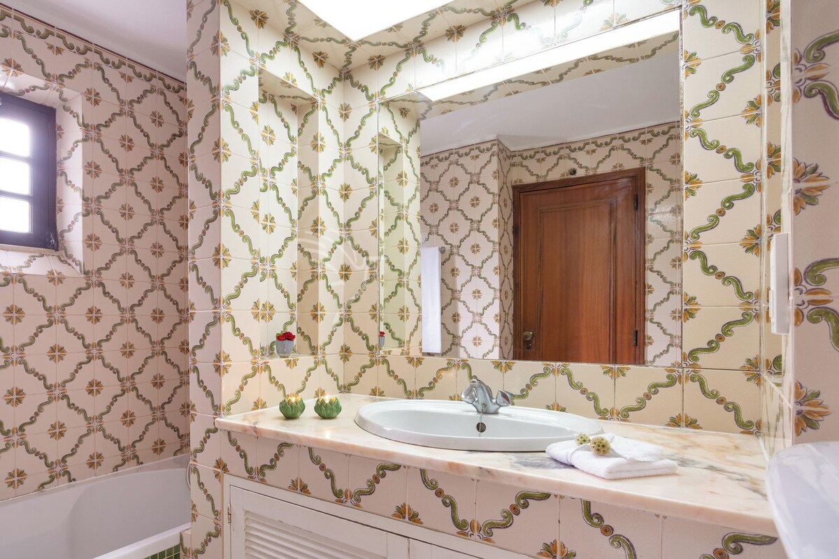A bathroom with patterned tiles, a bathtub, a sink with a mirror, and a window.