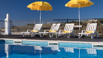 A poolside area with white lounge chairs and yellow umbrellas, a tiled pool, and a metal fence.