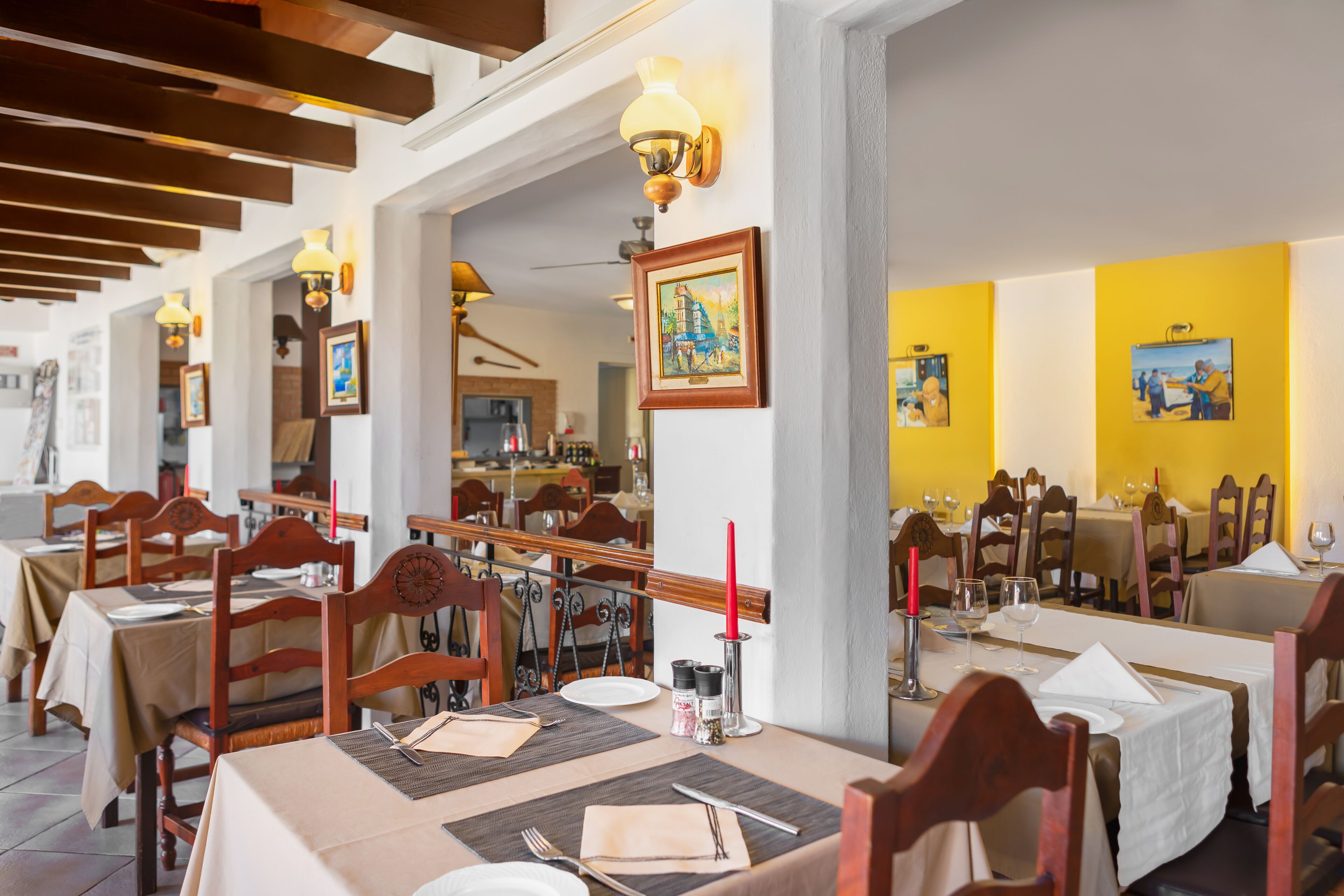 Un restaurante con mesas de madera, manteles blancos y cuadros decorativos en las paredes.