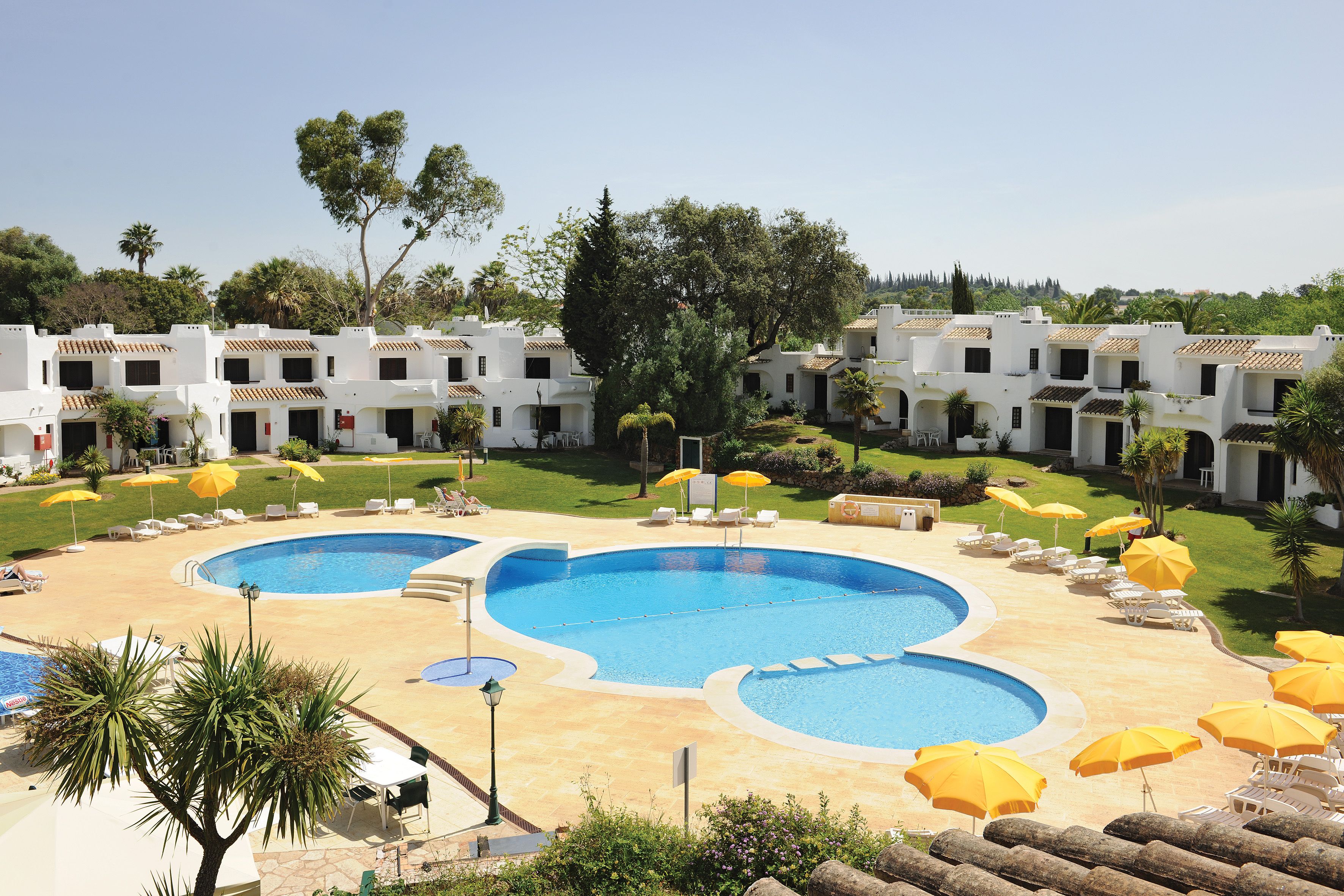 Un complex turístic amb diverses piscines, gandules i ombrelles.