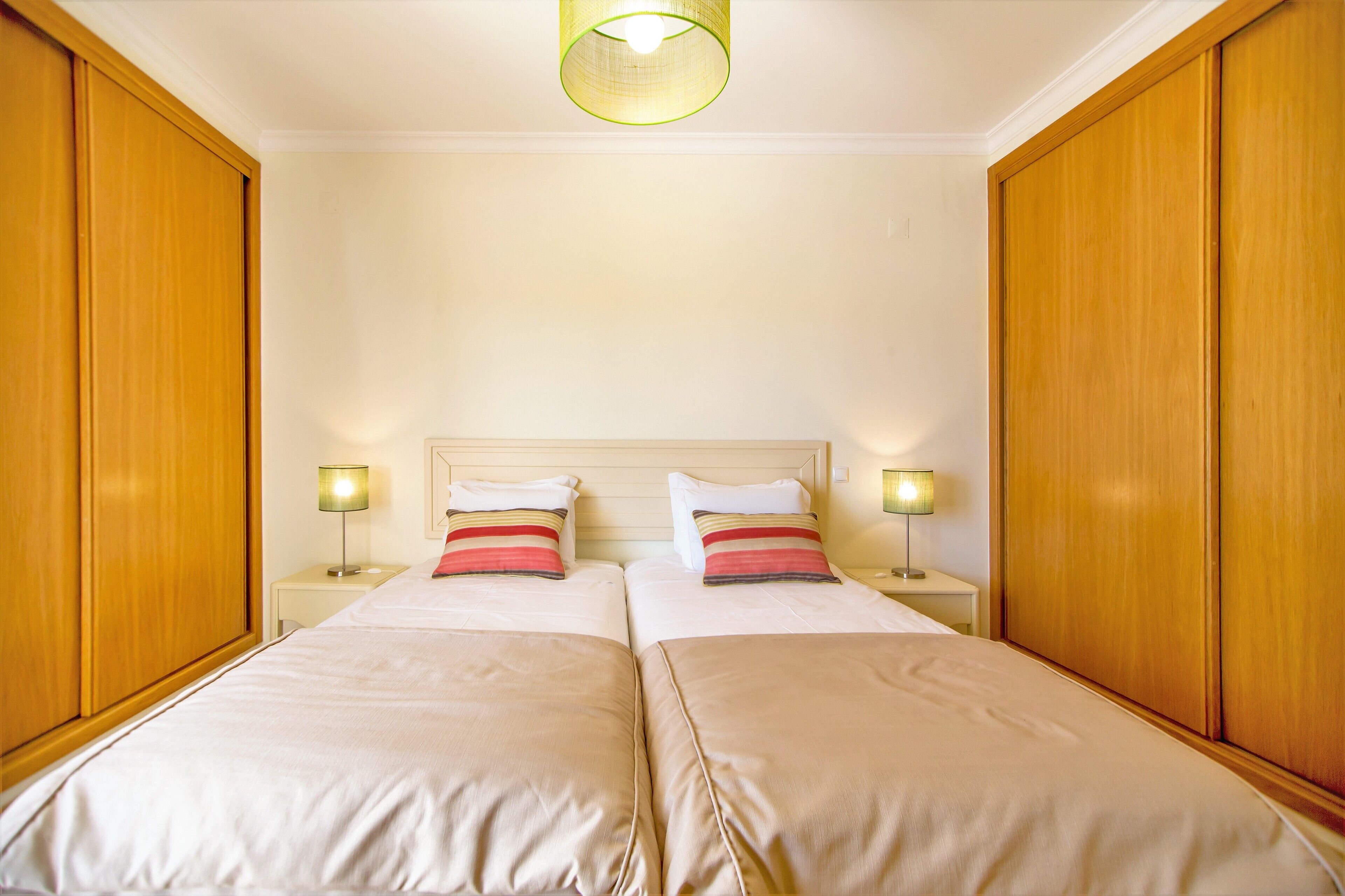 Hotellihuone, jossa on kaksi sänkyä, puiset vaatekaapit ja yöpöytävalaisimet.
