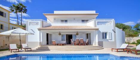 A two-story house with a pool, outdoor seating, and a clear blue sky.