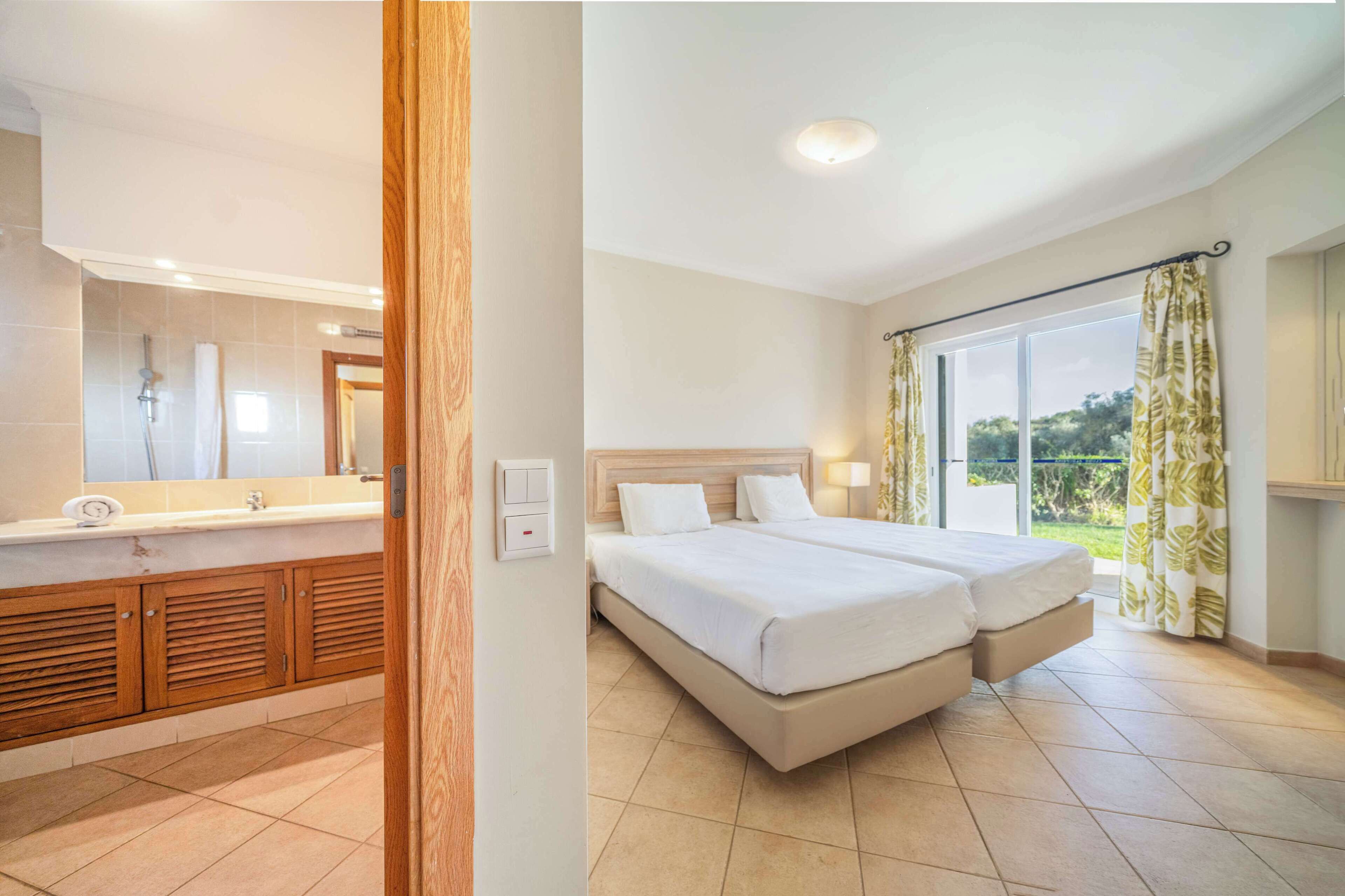 Habitación de hotel con baño, cama doble, ventana grande con cortinas y vista a zonas verdes.