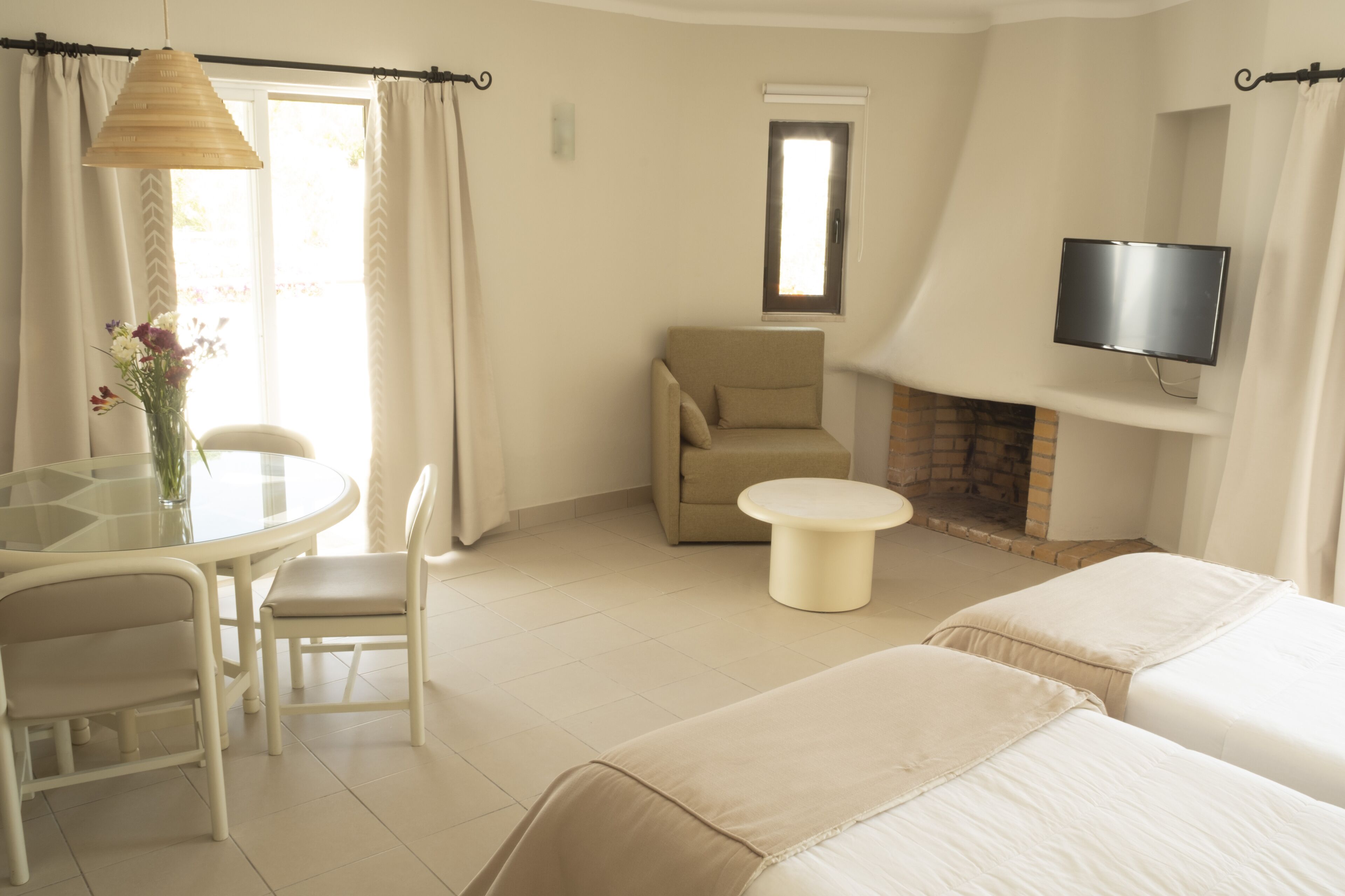 A hotel room with a dining table, chairs, a sofa, a TV, and a fireplace.