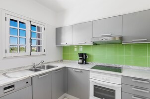 Una cocina moderna con armarios grises, encimera blanca, salpicadero verde y ventana con marcos blancos.