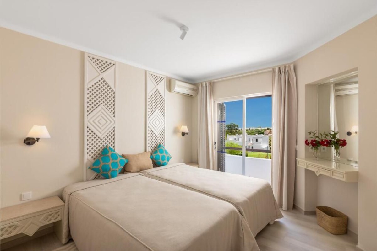 A hotel room with two beds, a balcony with a view, and a mirror above the vanity.