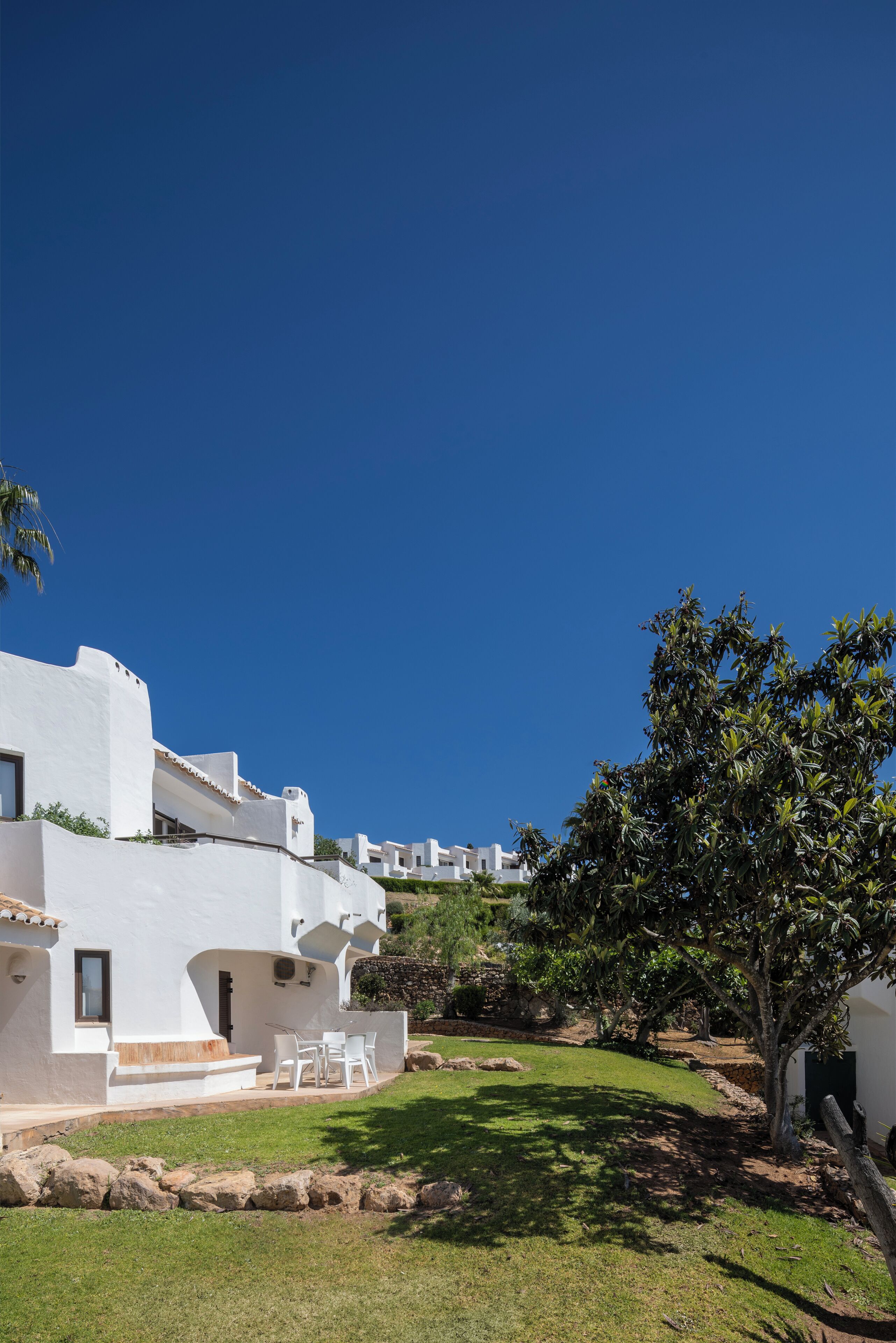 A white villa with a patio, a tree, and a clear blue sky.