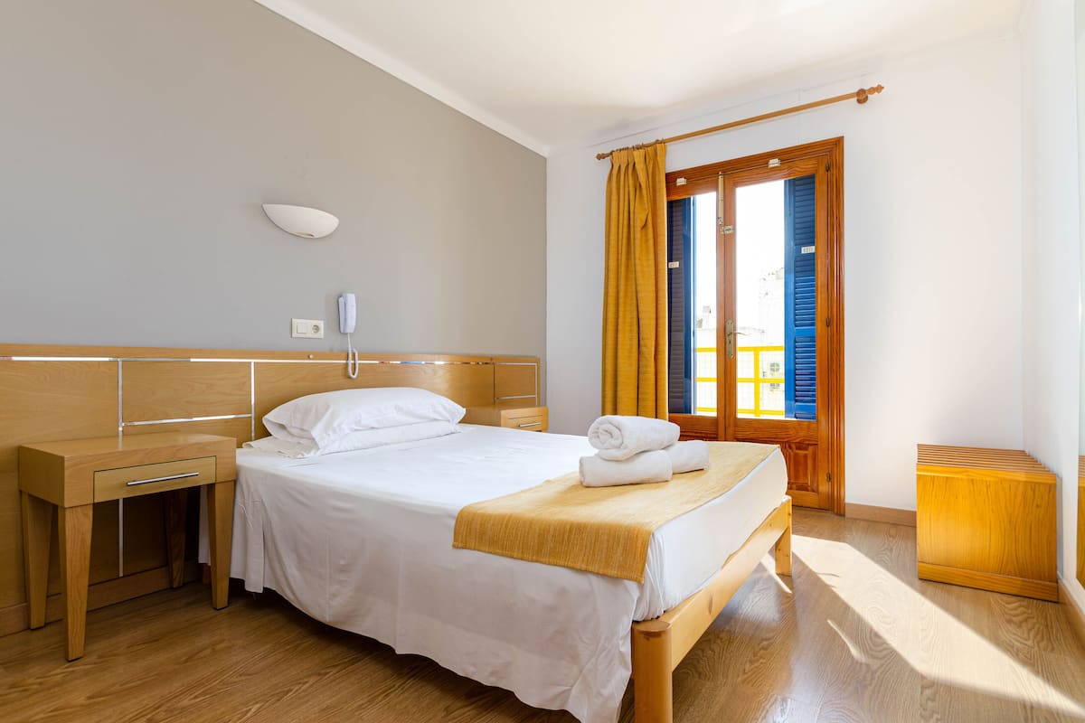 A neatly arranged hotel room with a bed, bedside table, and a small wooden cabinet.