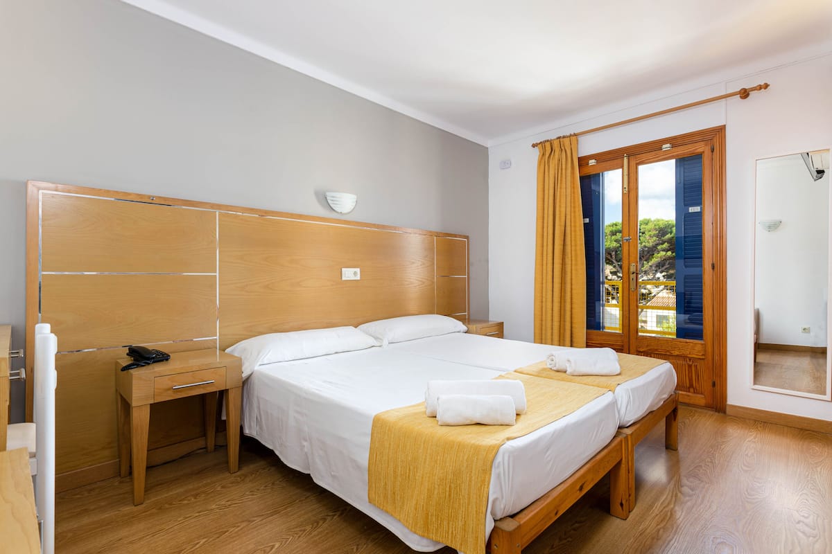 A neatly arranged hotel room with a large bed, a bedside table with a phone, and a window with curtains.