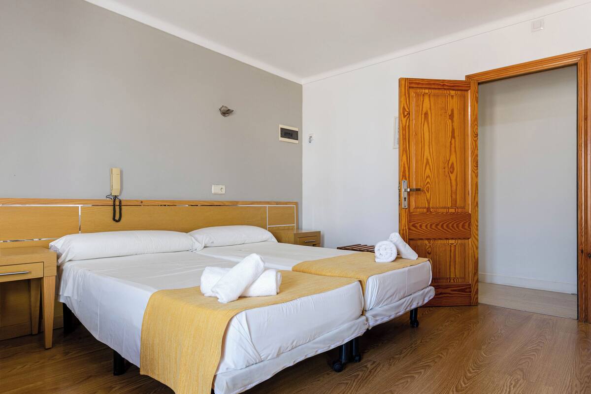 A double room with two beds, wooden headboards, a wooden door, and a bedside table with a lamp.