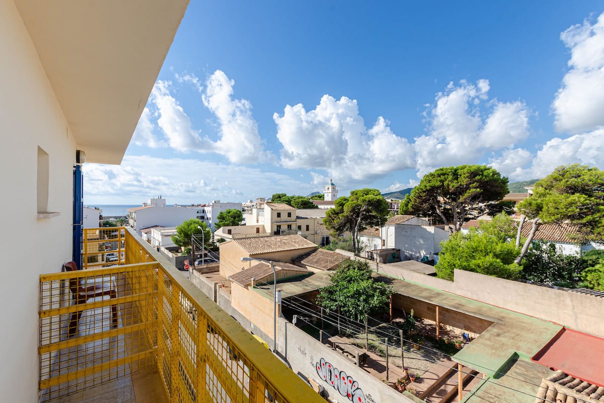 A high-rise building with a yellow railing, a view of a town with buildings and trees, and a clear sky.