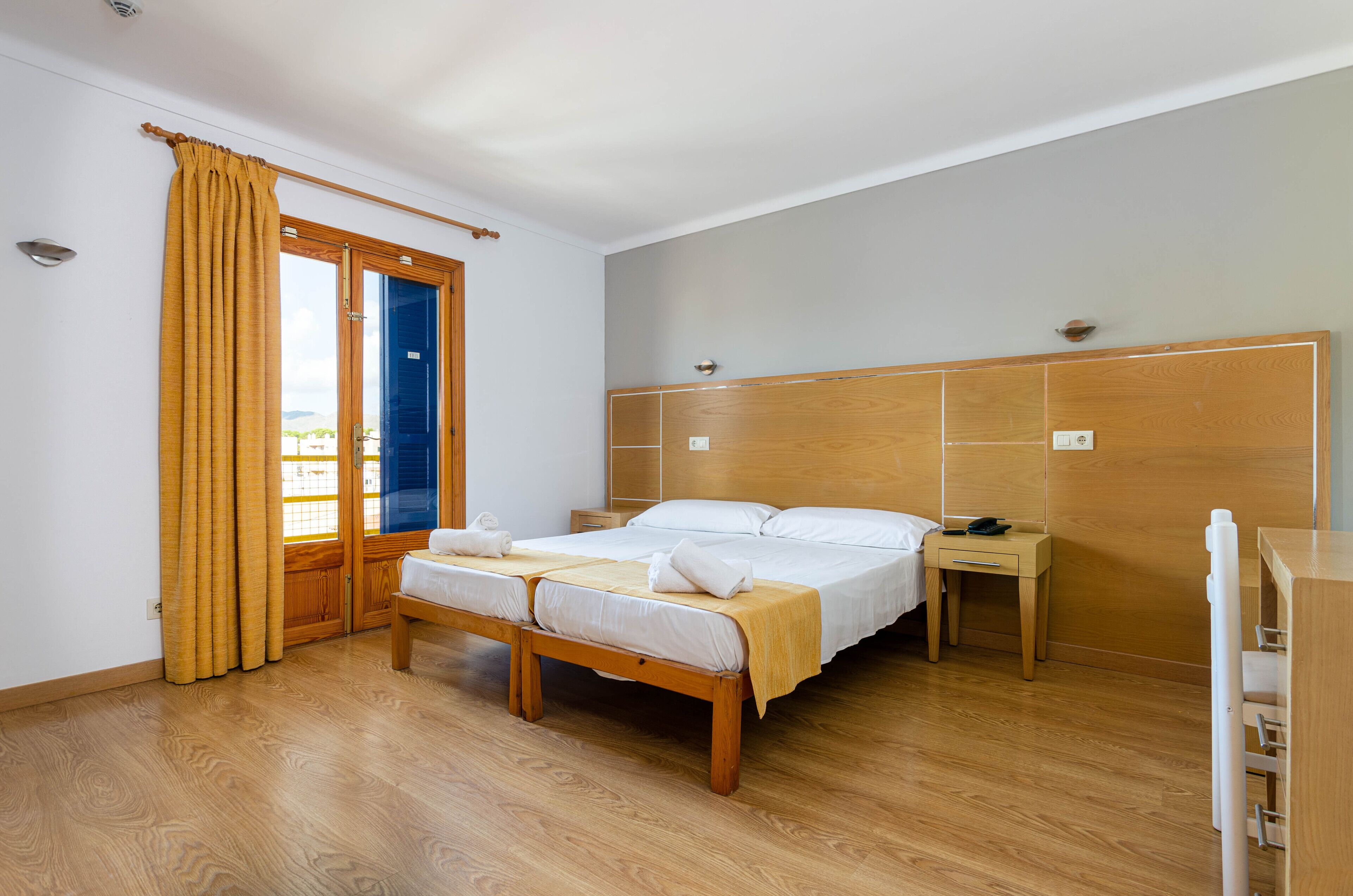 Een slaapkamer met een houten bed, een nachtkastje, een houten kledingkast en een raam met gordijnen.