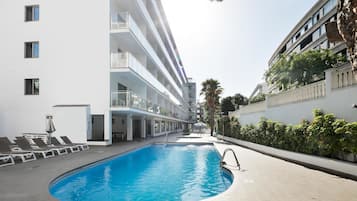 Una piscina amb gandules i una zona d'estar coberta, envoltada per un edifici de diversos pisos amb balcons.