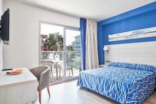 A modern hotel room with a large bed, a desk with a plate of fruit, a chair, and a view of the outside balcony. - Hotel Best Los Angeles (Salou)