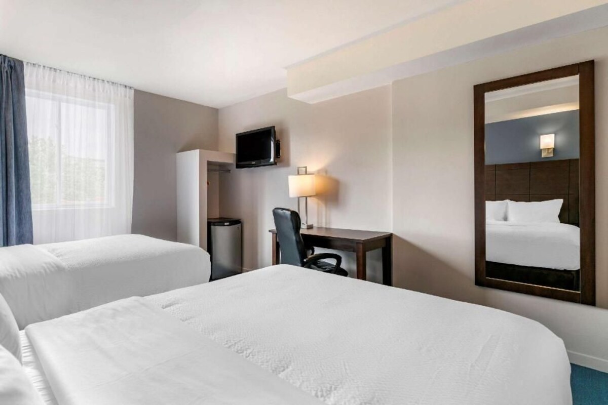 A hotel room with two beds, a TV, a desk with a chair, a lamp, and a large mirror.