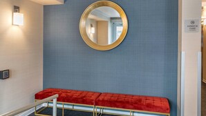 A hotel reception area with a red bench, a round mirror, and a sign indicating the entrance to the hotel lobby. - Econo Lodge (Montreal)