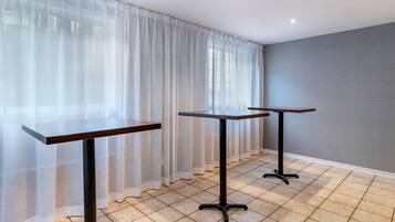 A room with two tables, a large window with sheer curtains, and a tiled floor.
