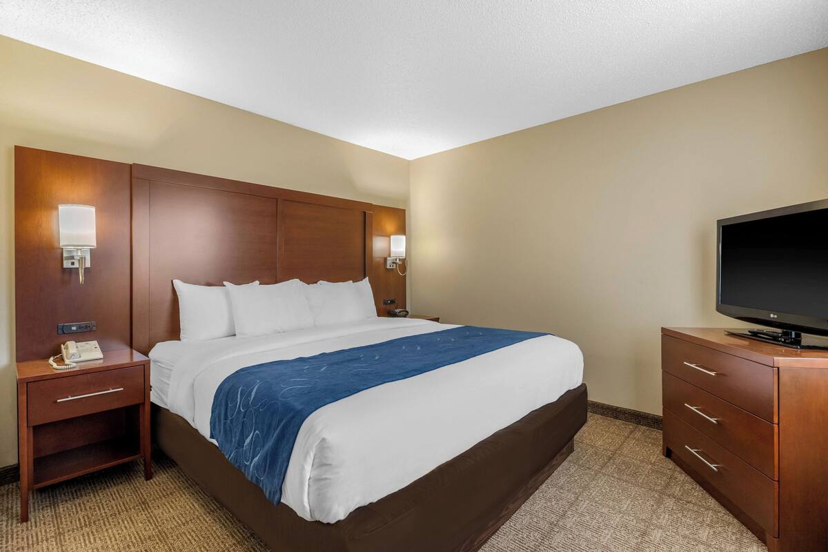 Una camera d'hotel con un letto grande, una testiera in legno, una televisione a schermo piatto, un comodino e un armadio.