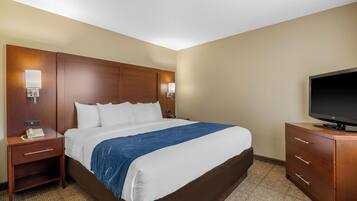 A hotel room with a large bed, a wooden headboard, a flat-screen TV, a nightstand, and a dresser.
