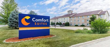 Señal de Comfort Suites con un edificio moderno al fondo.