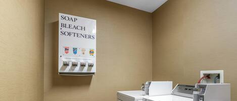 A laundry area with a sign for soap, bleach, and softeners, and a washing machine.