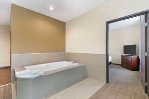 A modern bathroom with a large bathtub, a vanity with a mirror, and a television in the adjacent room.