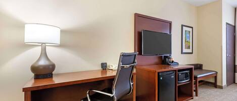A hotel room with a desk, chair, television, refrigerator, microwave, and a small bench.