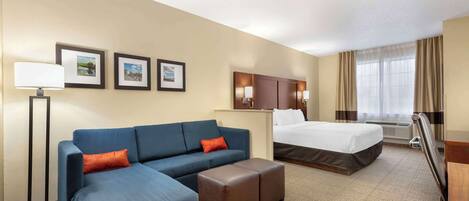 A hotel room with a large bed, a sofa, a desk, and a lamp.