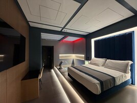 Moderni hotellihuone, jossa on suuri sänky, televisio, työpöytä ja oleskelualue.