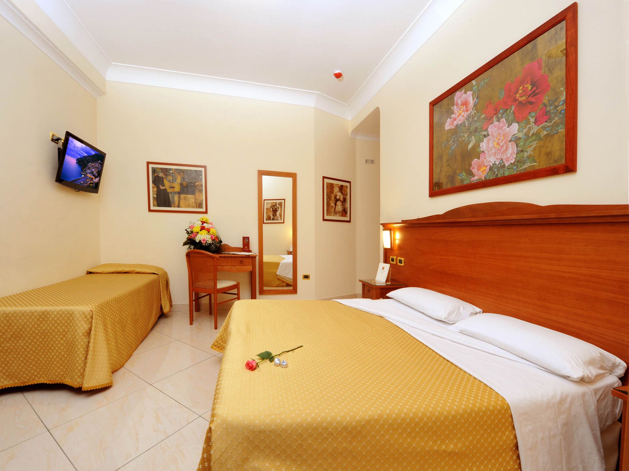 A hotel room with a bed, a desk, a chair, a TV, and a painting on the wall.