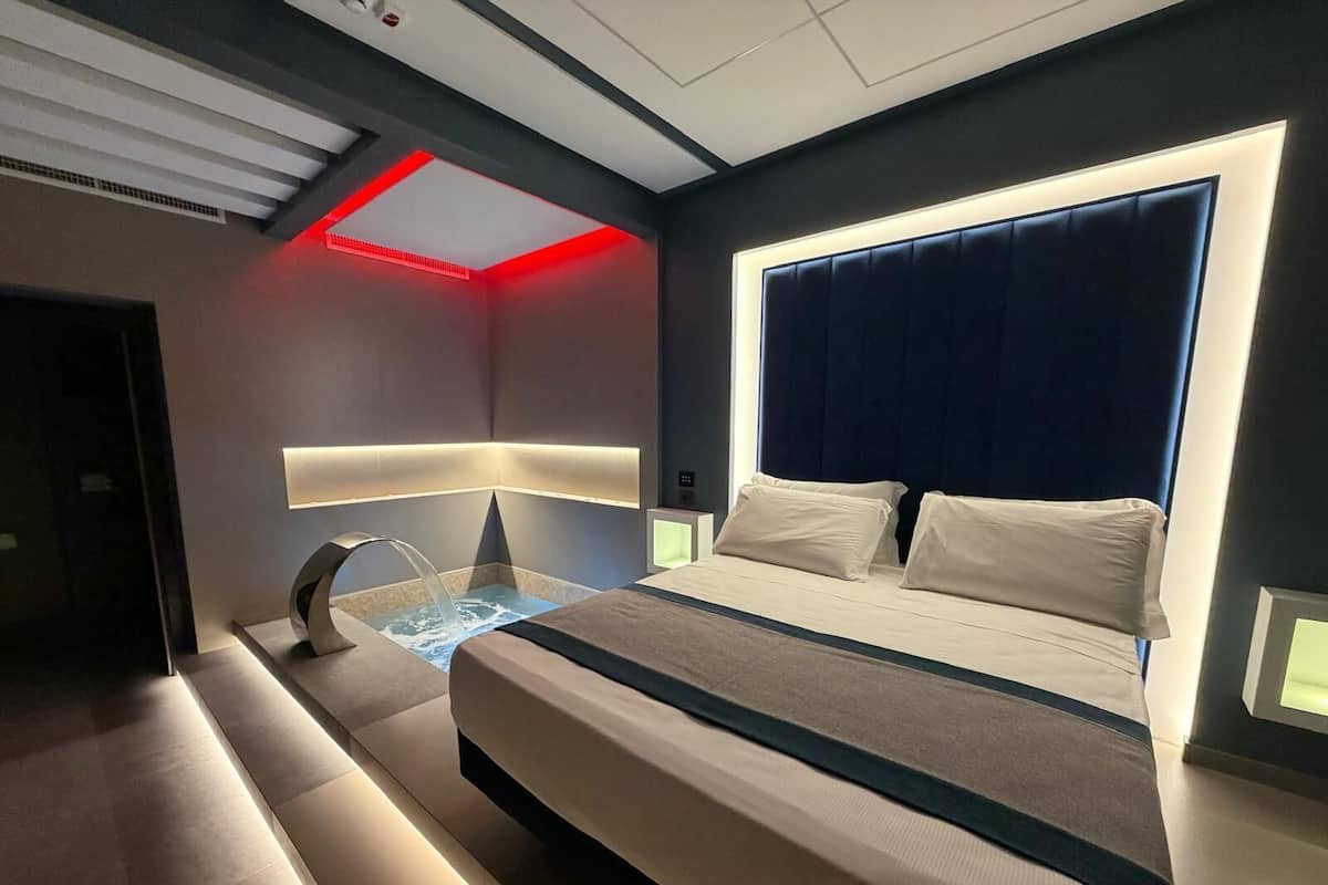 A modern hotel room with a bed, a built-in water feature, and a unique ceiling design.