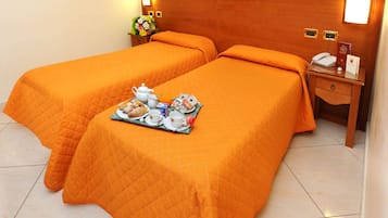 Habitación de hotel con dos camas, cada una con colcha naranja, una mesita de noche con teléfono y reloj, y una bandeja con alimentos para el desayuno.