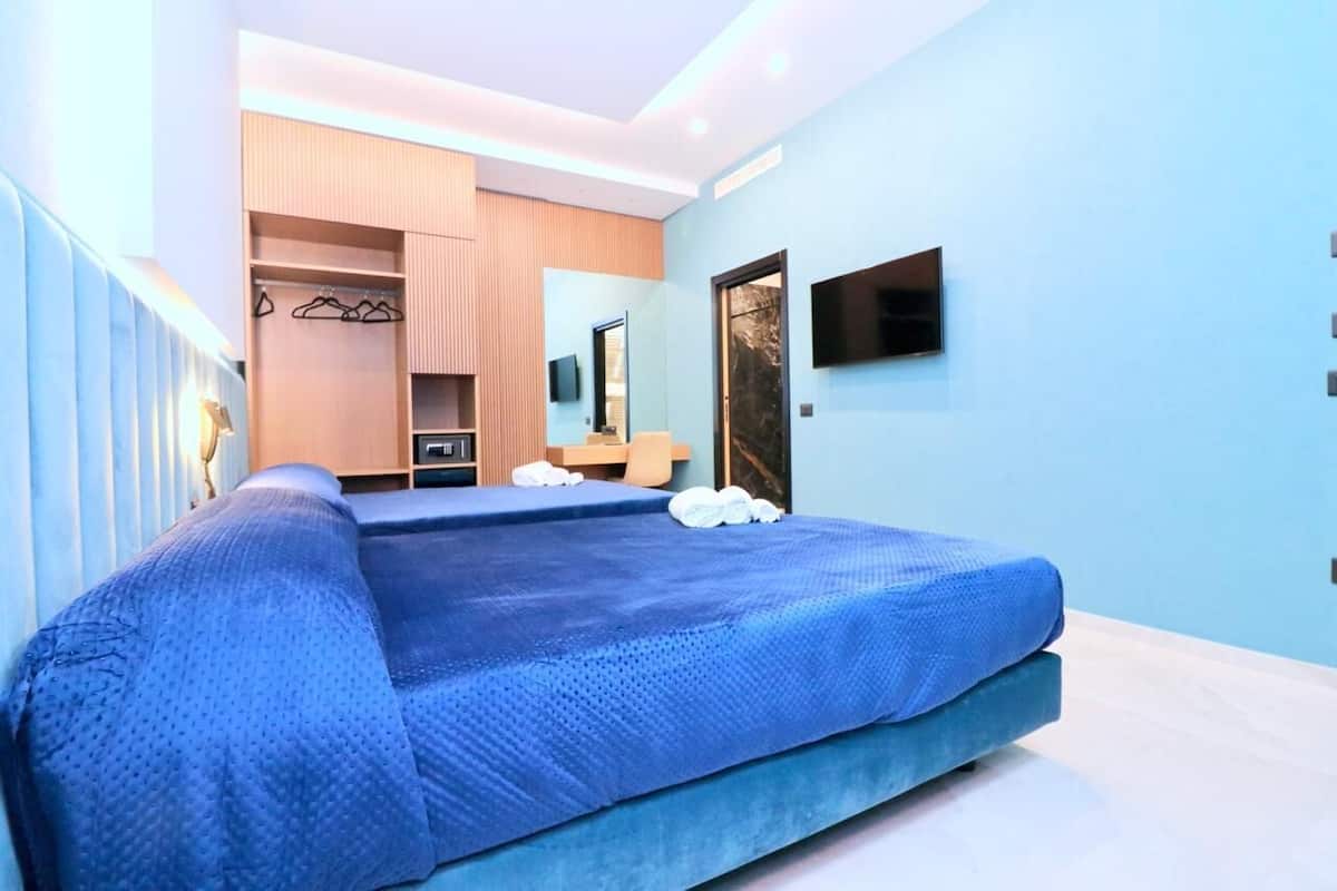A modern bedroom with a large bed, a wardrobe, a mirror, and a TV mounted on the wall.