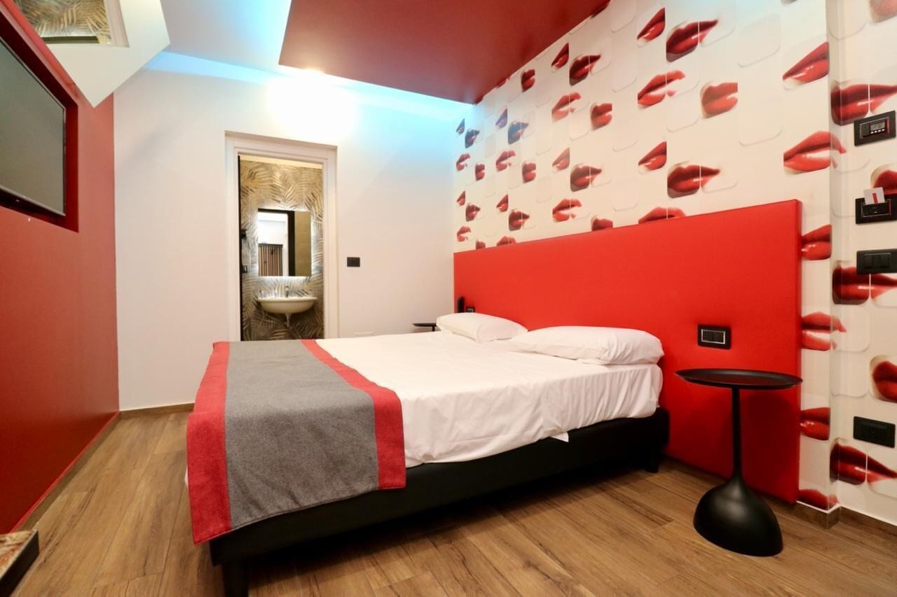 Un dormitori amb un llit, una paret vermella decorativa, un mirall, un lavabo i una paret amb dibuixos de llavis.