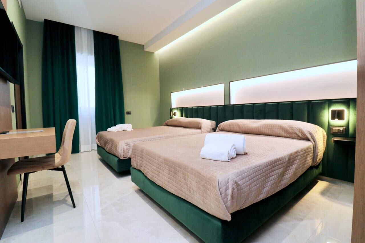 Une chambre d’hôtel avec deux lits, un bureau, une chaise et une grande fenêtre avec des rideaux.